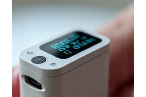 Advanced health monitor on a person's finger, displaying heart rate and blood oxygen levels.